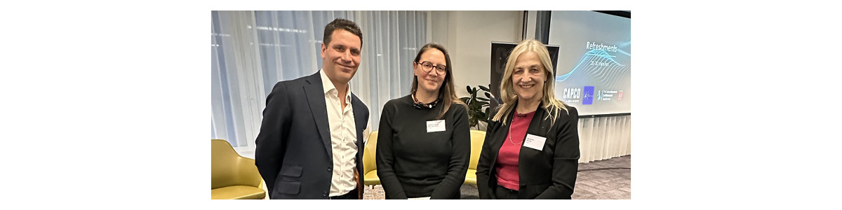Three professionals networking at Capco event with presentation screen in background